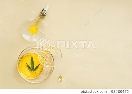 CBD oil in a pipette, THC tincture in laboratory round cups and marijuana leaves on light background CBD oil in a pipette, THC tincture in laboratory round cups and marijuana leaves on light background 92380475