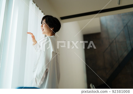 A young woman who opens a curtain A young woman who opens a curtain 92381008