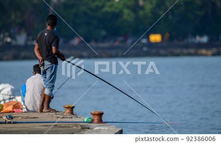 two men fishing at the peer, using fishing rods. two men fishing at the peer, using fishing rods. 92386006