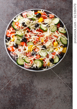 Shopska salad with tomatoes, cucumbers, onions, bell peppers, olives and cheese close-up in a plate. Vertical top view 92386470