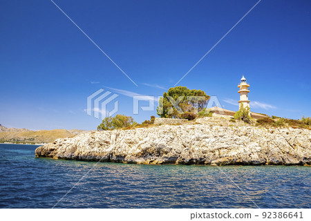 Lighthouse in Port de Pollenca on cliff by Mediterranean sea against blue sky 92386641