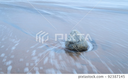 Isolated rock on the sandy beach, beach waves going back around the rock long exposure photograph, 92387145
