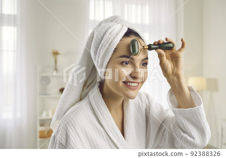 Beautiful young woman doing face massage with facial roller for better blood circulation 92388326