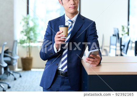 A young businessman in a suit operating a smartphone while taking a break 92392165