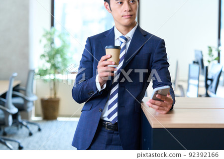 A young businessman in a suit operating a smartphone while taking a break 92392166
