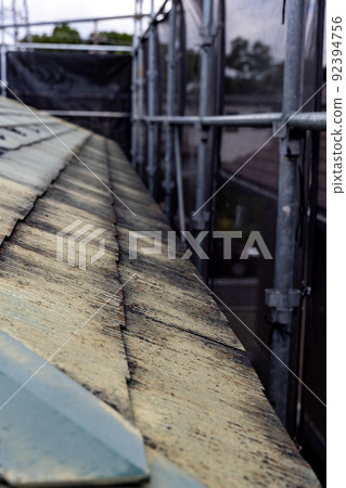 A scaffolding for the re-roofing of a faded and dirty roof of a 25-year-old single-family home A scaffolding for the re-roofing of a faded and dirty roof of a 25-year-old single-family home 92394756