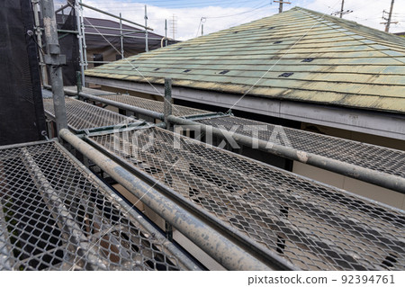 A scaffolding for the re-roofing of a faded and dirty roof of a 25-year-old single-family home 92394761
