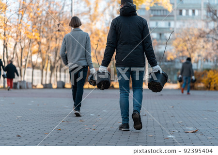 volunteers carrying young tree sapling in pots for planting in city park 92395404