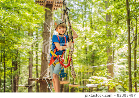 Happy child in a helmet, healthy teenager school boy enjoying activity in a climbing adventure park on a summer day Portrait of a disgruntled girl sitting at a cafe table 92395497