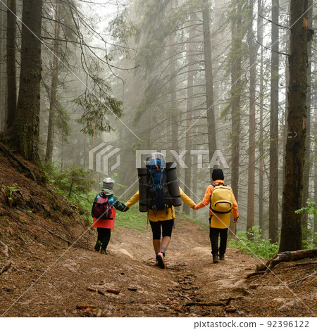 Mother with two children and backpacks in the forest, hiking with children, tourists in the fog between tall trees. Mother with two children and backpacks in the forest, hiking with children, tourists in the fog between tall trees. 92396122