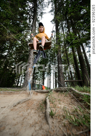 A boy swings on a swing somewhere in the forest. 92396165