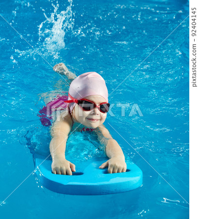 Little girl learning to swim in indoor pool with pool board Little girl learning to swim in indoor pool with pool board 92404145
