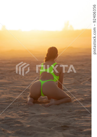 Seductive model in swimsuit kneeling on sandy beach 92406356