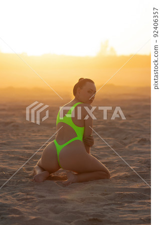 Seductive model in swimsuit kneeling on sandy beach 92406357