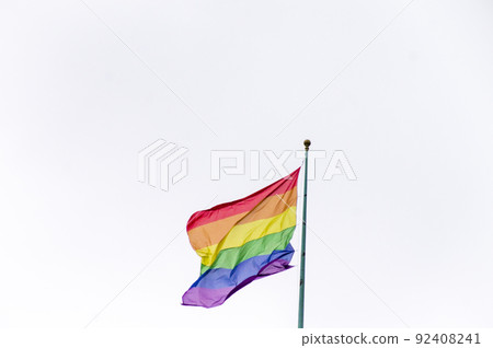 Close Up rainbow gay pride flag outside on a street. Symbol of the Lesbian Bisexual Transgender LGBT community waving in wind against cloudy sky. Social movement for freedom and equliaty. Copy Space 92408241