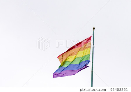 Close Up rainbow gay pride flag outside on a street. Symbol of the Lesbian Bisexual Transgender LGBT community waving in wind against cloudy sky. Social movement for freedom and equliaty. Copy Space 92408261