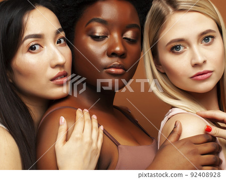 young pretty african and caucasian women posing cheerful together on brown background, lifestyle diverse nationality people concept close up 92408928
