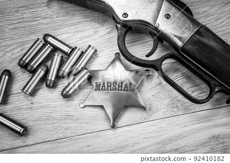 Old west repeating rifle with ammunition and marshals badge. Black and white photo. 92410182