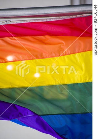 Close Up rainbow gay pride flag outside on a street. Symbol of the Lesbian Bisexual Transgender LGBT community waving in wind against cloudy sky. Social movement for freedom and equliaty. Copy Space 92410344