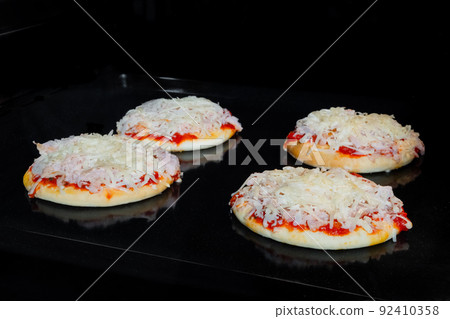Four homemade mini pizzas baking on tray in electric oven Four homemade mini pizzas baking on tray in electric oven 92410358