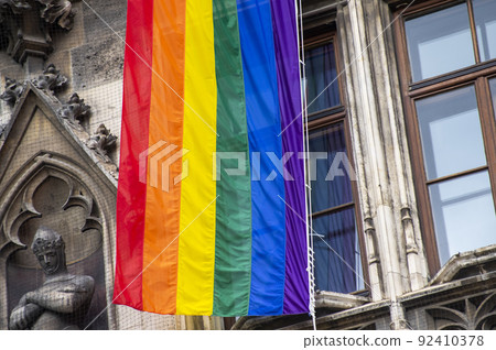 Close Up rainbow gay pride flag outside on a street. Symbol of the Lesbian Bisexual Transgender LGBT community waving in wind against cloudy sky. Social movement for freedom and equliaty. Copy Space 92410378