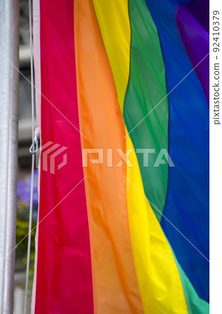 Close Up rainbow gay pride flag outside on a street. Symbol of the Lesbian Bisexual Transgender LGBT community waving in wind against cloudy sky. Social movement for freedom and equliaty. Copy Space 92410379
