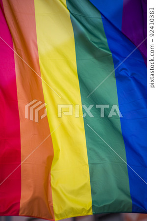Close Up rainbow gay pride flag outside on a street. Symbol of the Lesbian Bisexual Transgender LGBT community waving in wind against cloudy sky. Social movement for freedom and equliaty. Copy Space 92410381