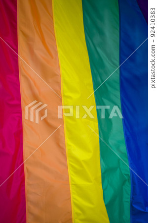Close Up rainbow gay pride flag outside on a street. Symbol of the Lesbian Bisexual Transgender LGBT community waving in wind against cloudy sky. Social movement for freedom and equliaty. Copy Space 92410383