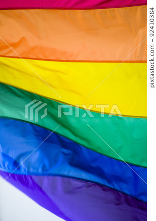 Close Up rainbow gay pride flag outside on a street. Symbol of the Lesbian Bisexual Transgender LGBT community waving in wind against cloudy sky. Social movement for freedom and equliaty. Copy Space 92410384