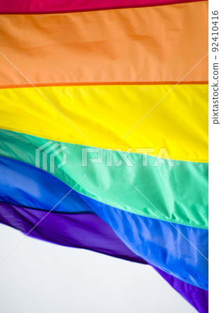 Close Up rainbow gay pride flag outside on a street. Symbol of the Lesbian Bisexual Transgender LGBT community waving in wind against cloudy sky. Social movement for freedom and equliaty. Copy Space 92410416