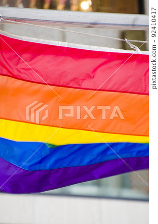 Close Up rainbow gay pride flag outside on a street. Symbol of the Lesbian Bisexual Transgender LGBT community waving in wind against cloudy sky. Social movement for freedom and equliaty. Copy Space 92410417