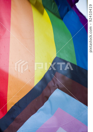 Close Up rainbow gay pride flag outside on a street. Symbol of the Lesbian Bisexual Transgender LGBT community waving in wind against cloudy sky. Social movement for freedom and equliaty. Copy Space 92410419