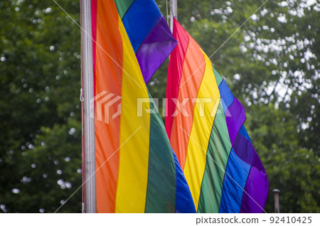 Close Up rainbow gay pride flag outside on a street. Symbol of the Lesbian Bisexual Transgender LGBT community waving in wind against cloudy sky. Social movement for freedom and equliaty. Copy Space 92410425