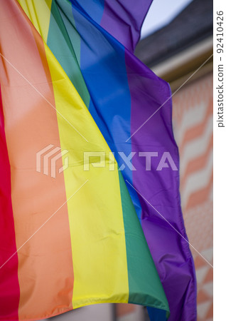 Close Up rainbow gay pride flag outside on a street. Symbol of the Lesbian Bisexual Transgender LGBT community waving in wind against cloudy sky. Social movement for freedom and equliaty. Copy Space 92410426