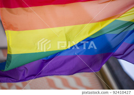 Close Up rainbow gay pride flag outside on a street. Symbol of the Lesbian Bisexual Transgender LGBT community waving in wind against cloudy sky. Social movement for freedom and equliaty. Copy Space 92410427