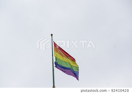 Close Up rainbow gay pride flag outside on a street. Symbol of the Lesbian Bisexual Transgender LGBT community waving in wind against cloudy sky. Social movement for freedom and equliaty. Copy Space 92410428