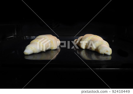 Two uncooked homemade croissants on tray in electric oven, black background Two uncooked homemade croissants on tray in electric oven, black background 92410449