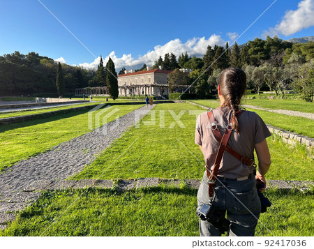 Girl photographer stands in the garden of Villa Milocer. Back view 92417036