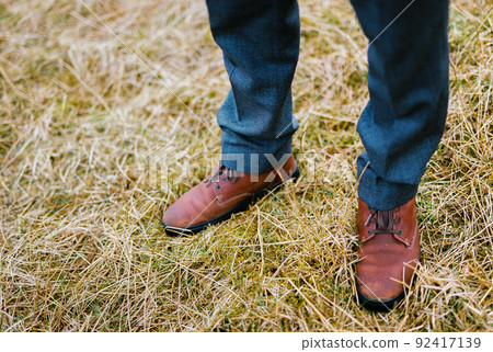 Men feet in brown shoes on dry grass. Close-up 92417139