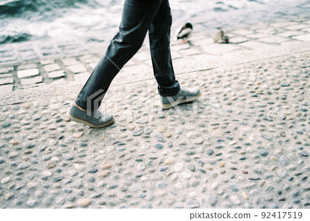 Men feet in sneakers walk along the paving stones Men feet in sneakers walk along the paving stones 92417519
