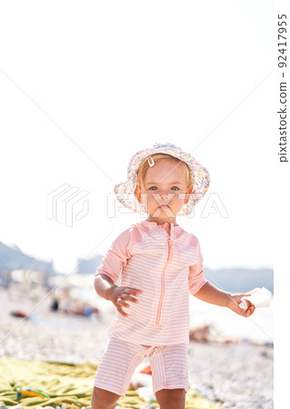 Little girl in a panama hat stands on a beach 92417955