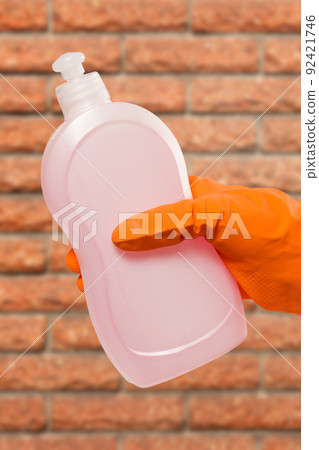 Woman's hand in protective glove with bottle of cleaning liquid. Woman's hand in protective glove with bottle of cleaning liquid. 92421746