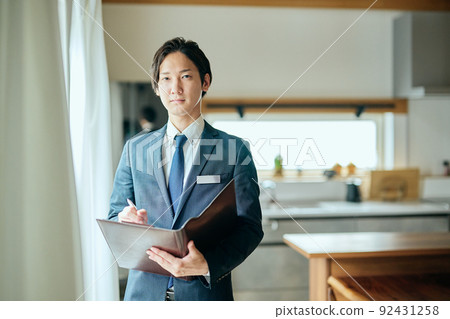 A home sales businessman standing in front of the kitchen with a leather binder 92431258