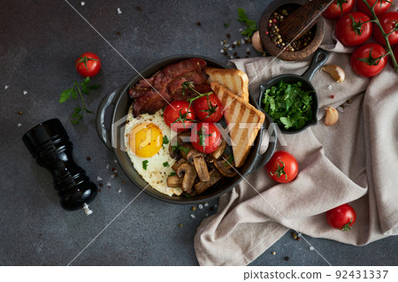 Fried eggs, bacon, tomato and toasted bread in a black ceramic pan at domestic kitchen Fried eggs, bacon, tomato and toasted bread in a black ceramic pan at domestic kitchen 92431337
