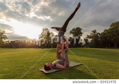 Healthy man lying on grass and balancing woman. Couple doing acrobatic yoga exercise in park Healthy man lying on grass and balancing woman. Couple doing acrobatic yoga exercise in park 92431470