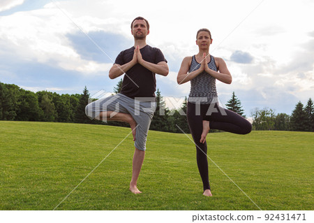 Full length view of a young couple doing the tree yoga pose together at a park 92431471