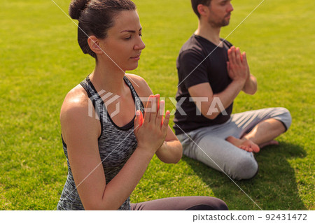 Young healthy man and woman doing yoga in the sunny summer park 92431472