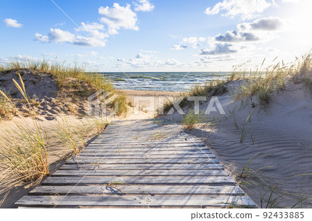 The path through dunes to the sandy beach on the Baltic Sea in summer with a blue sky The path through dunes to the sandy beach on the Baltic Sea in summer with a blue sky 92433885