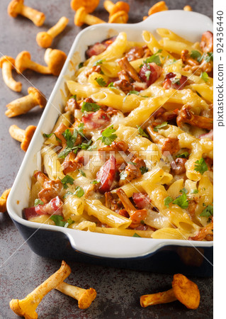 Penne pasta casserole with chanterelle mushrooms, meat and cheese close-up in a baking dish. vertical 92436440