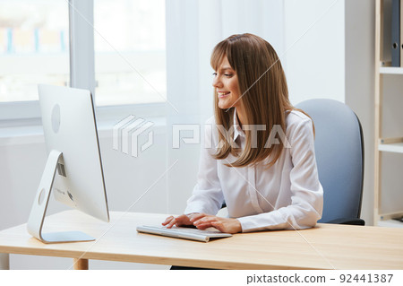 Cheerful happy adorable blonde businesswoman worker freelancer look at screen work on desktop computer online in light modern office. Happy employee typing quarterly report. Copy space, remote job Cheerful happy adorable blonde businesswoman worker freelancer look at screen work on desktop computer online in light modern office. Happy employee typing quarterly report. Copy space, remote job 92441387